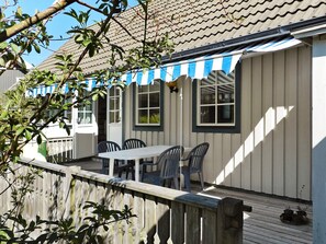 A covered outdoor seating area with a table and chairs, a wooden deck, and a building with windows and a striped awning. - Holiday Home in Lysekil (Lysekil)