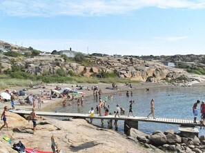 A rocky beach with people swimming and walking on a wooden pier. - Holiday Home in Lysekil (Lysekil)