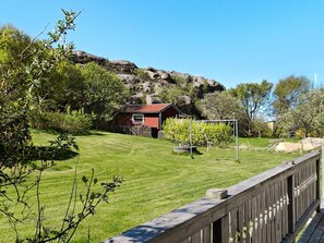 En rødmalede bygning med skråt tag, omgivet af en velplejet græsplæne og træer.