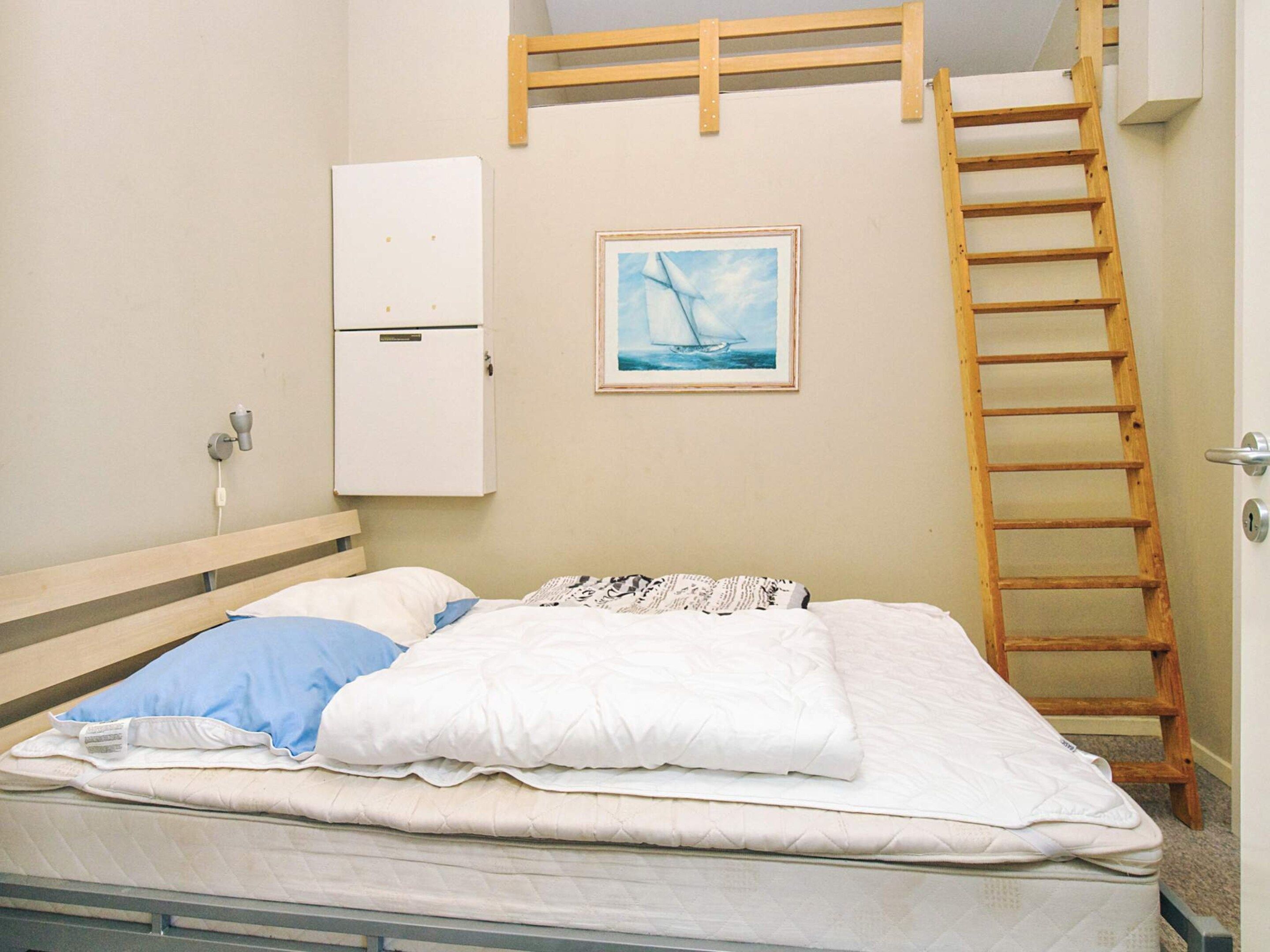 A single bed with a mattress, pillows, a wooden ladder, a white cabinet, and a framed picture on the wall.