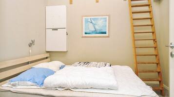 A single bed with a mattress, pillows, a wooden ladder, a white cabinet, and a framed picture on the wall.