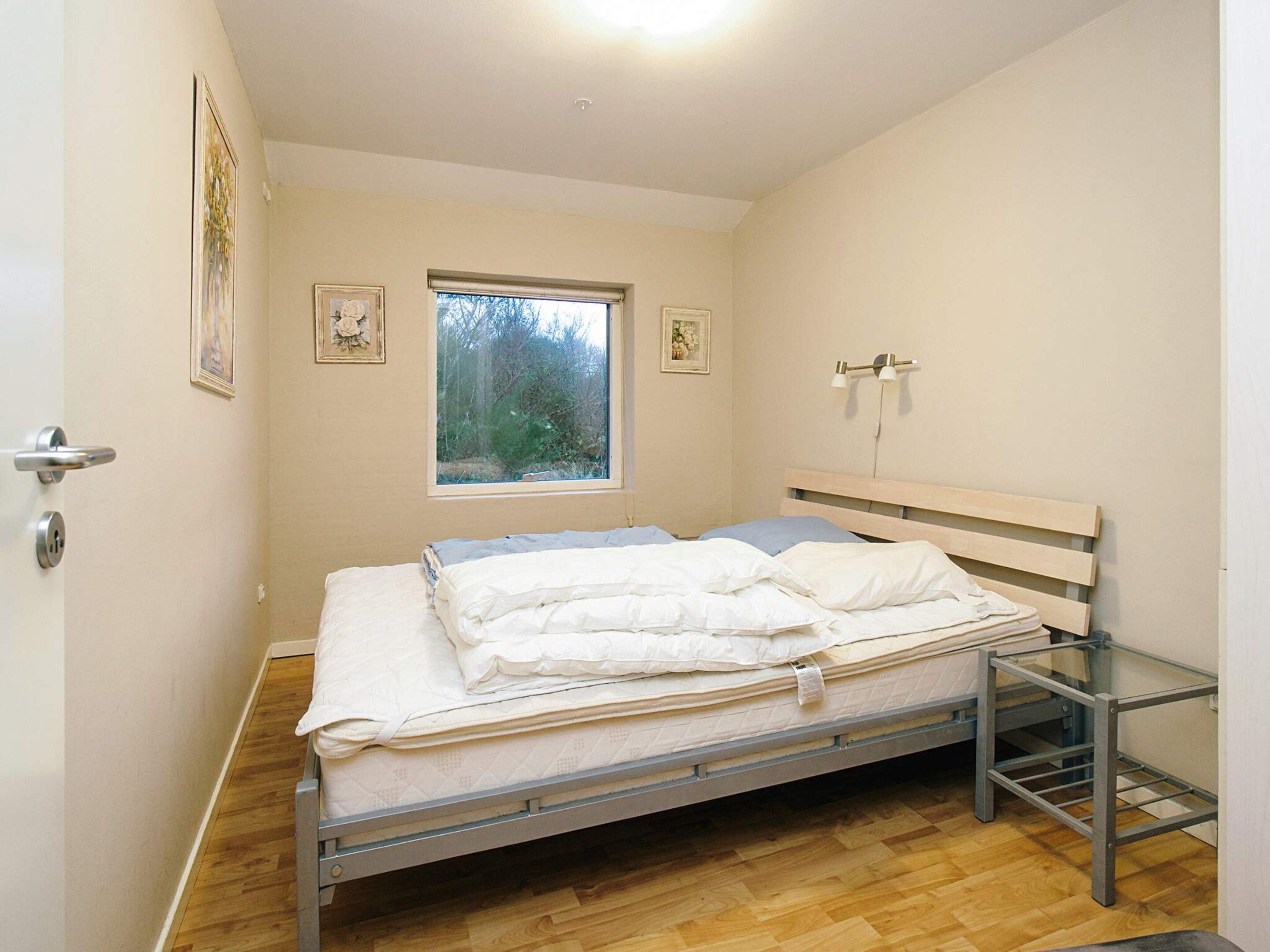 A bedroom with a bed, a window, a door, and a wall-mounted light fixture.