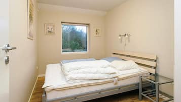A bedroom with a bed, a window, a door, and a wall-mounted light fixture.