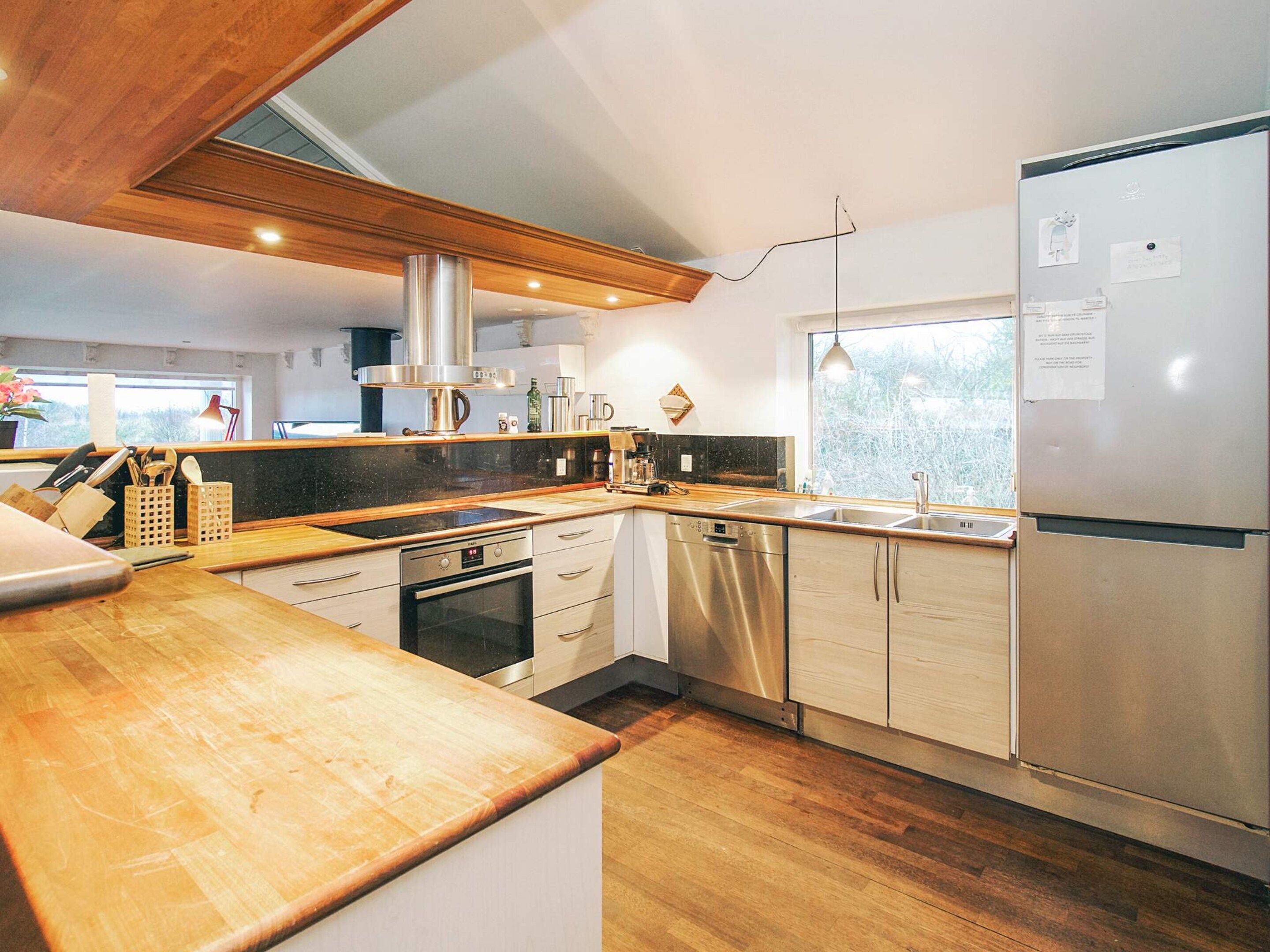 A modern kitchen with stainless steel appliances, wooden countertops, and a large window.