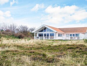 Una casa costanera amb façana blanca, grans finestres i teulada de teules vermelles.