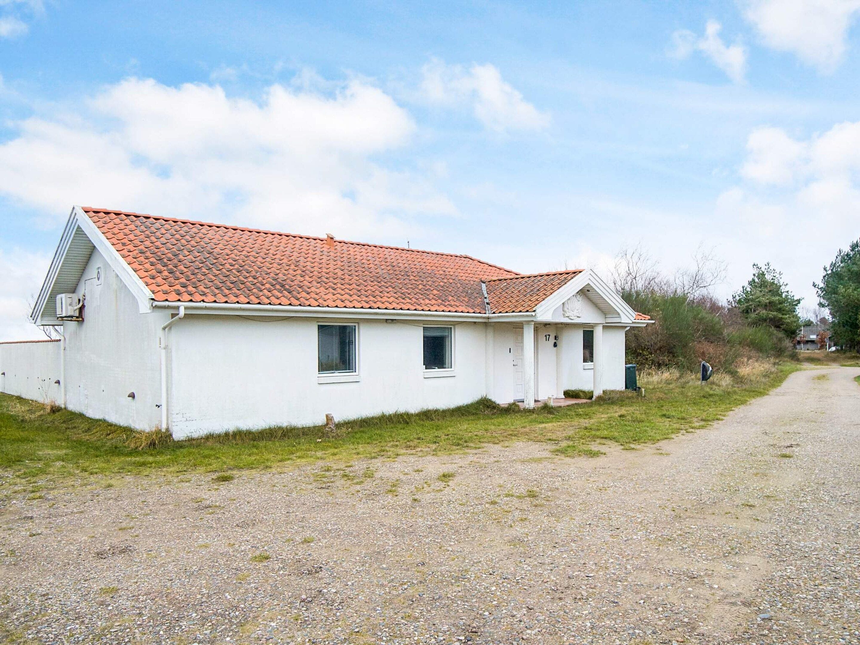 A white building with a red-tiled roof, a gravel driveway, and a grassy area.