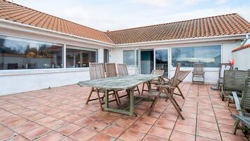 A patio with a table and chairs, a tiled roof, and large windows.