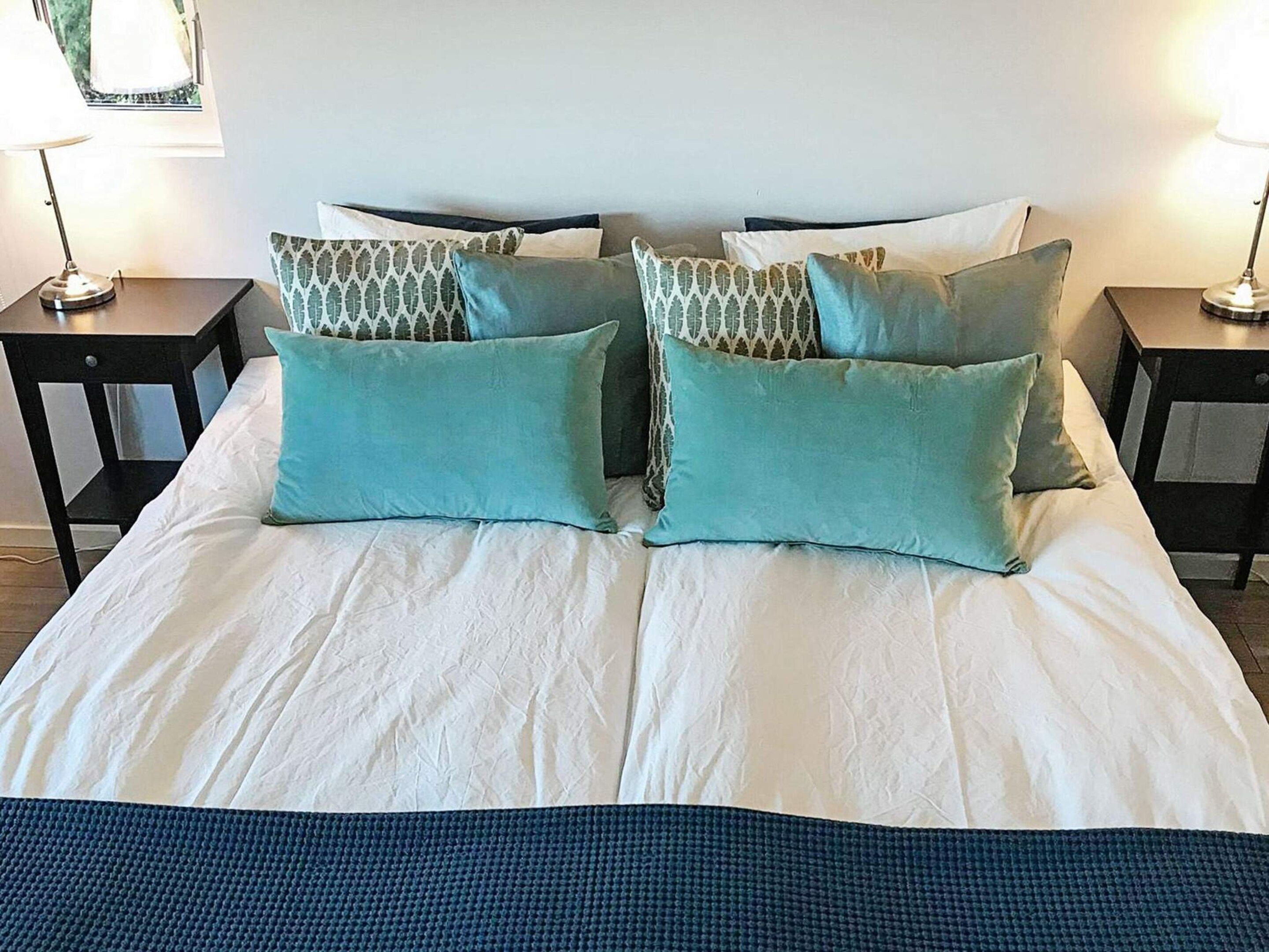 A bed with white bedding and multiple pillows, two bedside tables, and a lamp on each side.