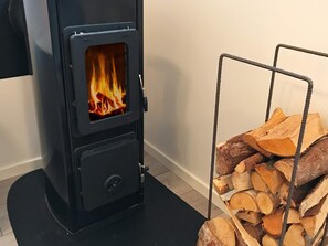 A wood-burning stove with visible flames, a black exterior, and a metal rack holding firewood. - 4 Star Holiday Home in Akersberga (Akersberga)