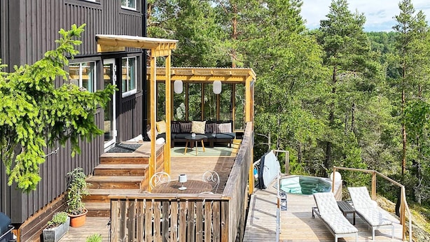 A wooden deck with a hot tub, outdoor seating, and a view of a forest. - 4 Star Holiday Home in Akersberga (Akersberga)