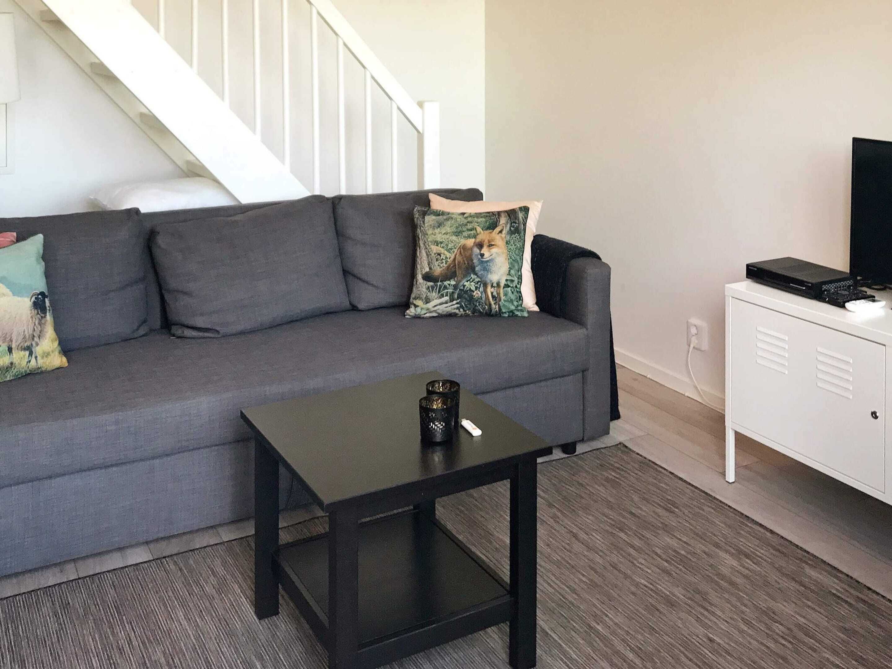 A living room with a grey sofa, a small black table, a white cabinet, and a staircase in the background.