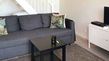 A living room with a grey sofa, a small black table, a white cabinet, and a staircase in the background.