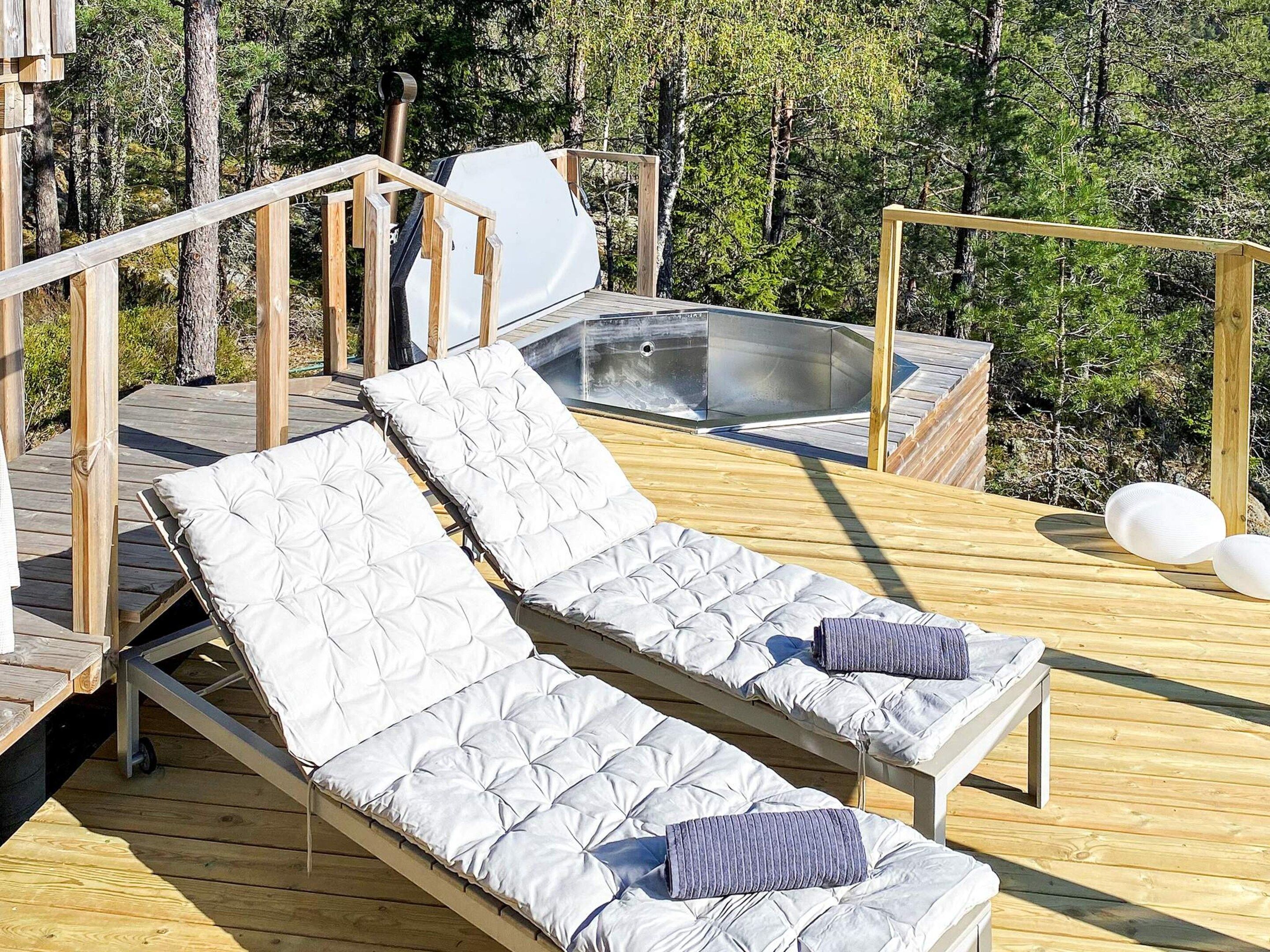 A wooden deck with two reclining lounge chairs, a hot tub, and a wooden railing.