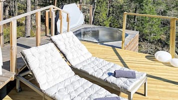 A wooden deck with two reclining lounge chairs, a hot tub, and a wooden railing.