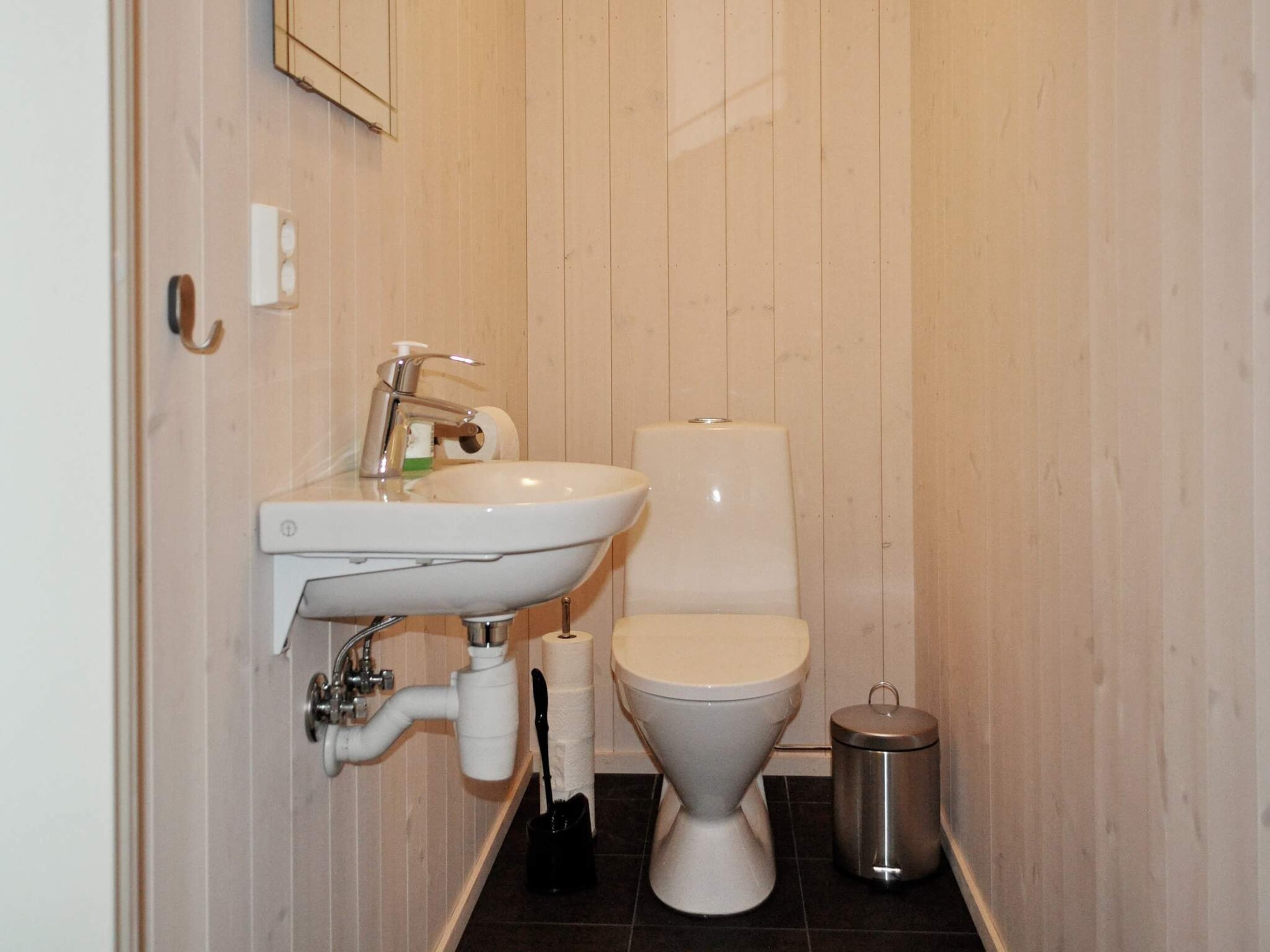 Un baño pequeño con lavamanos, inodoro y un cubo de basura blancos.