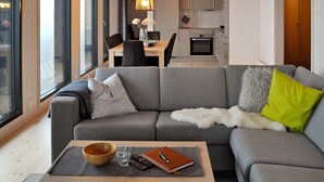 Uma sala de estar moderna com um sofá cinza, uma mesa de centro de madeira e uma área de jantar ao fundo.