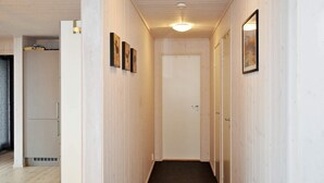 Um corredor estreito com paredes de madeira, chão de azulejos escuros e uma porta branca no final.