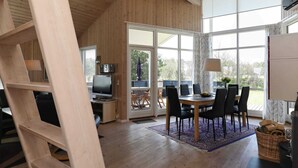 A spacious room with a wooden interior, a dining area with a table and chairs, a television, and a large window providing a view of the outdoors. - 4 Star Holiday Home in Ulfborg (Ulfborg)