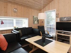 Un salon moderne avec un canapé en cuir noir, une table basse en bois, un fauteuil noir, un grand téléviseur à écran plat et une horloge murale.