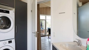A modern laundry room with stacked washing machines, a large mirror, and a sink with a faucet. - 4 Star Holiday Home in Ulfborg (Ulfborg)