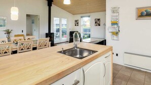 A modern kitchen with wooden countertops, a stainless steel sink, and white cabinetry. There is a dining area with wooden chairs and a table, and a large window providing natural light.