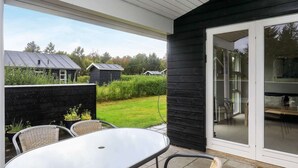A patio with a round table and wicker chairs, a black exterior wall, and a sliding glass door leading to an indoor area.