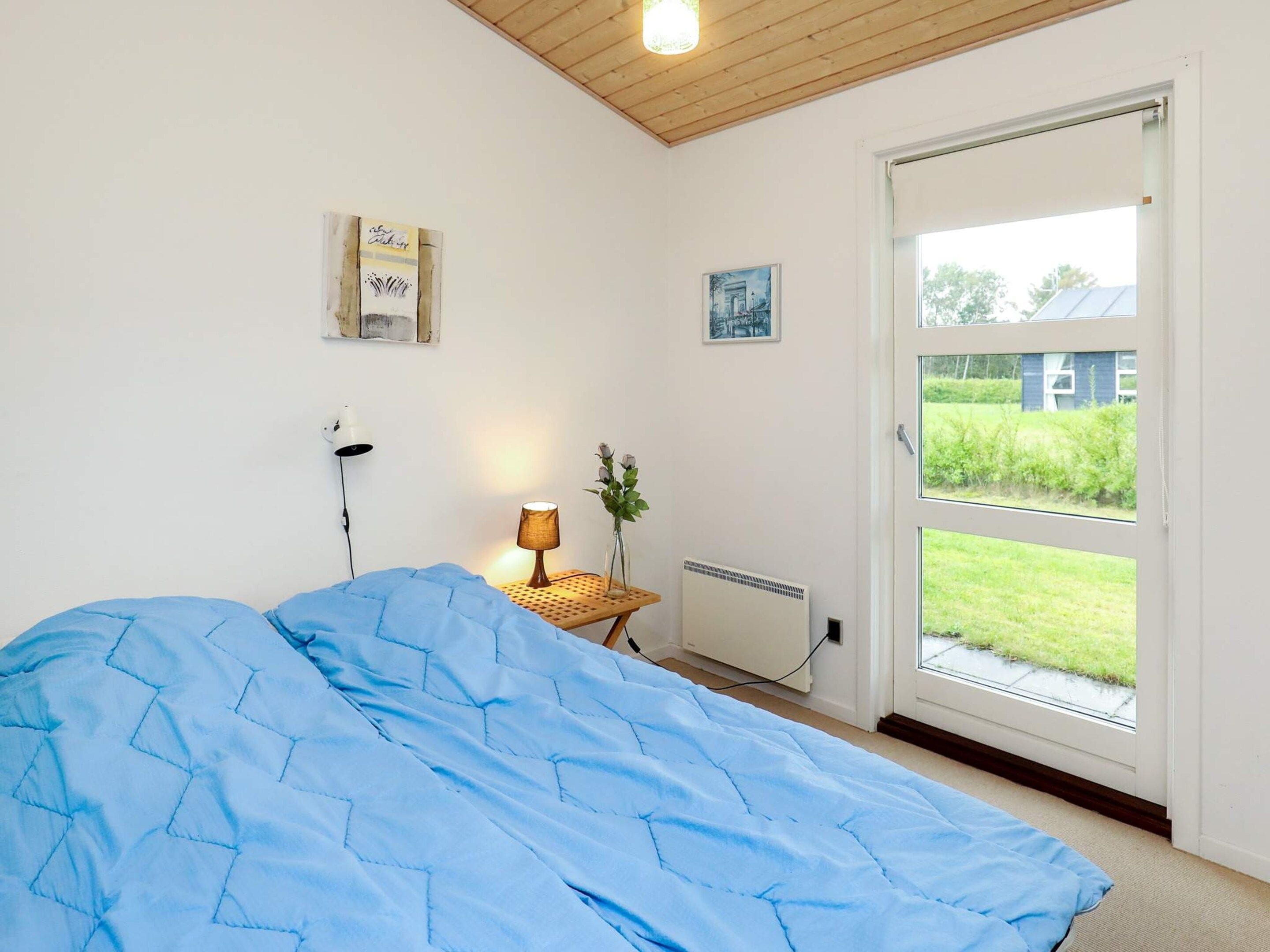 A bedroom with a bed, a bedside lamp, a radiator, and a view of the outdoors through a door.