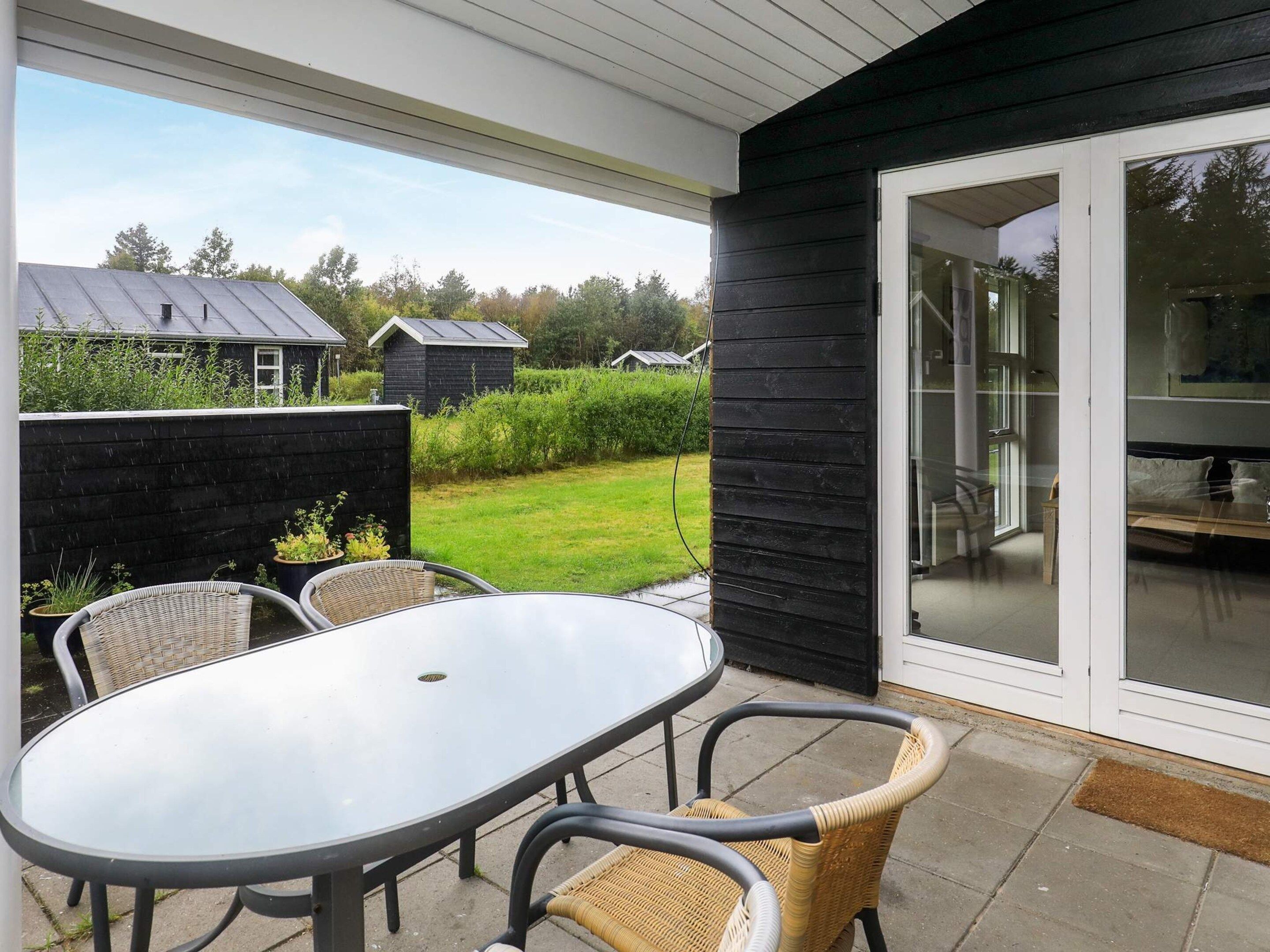 A patio with a round table and wicker chairs, a black exterior wall, and a sliding glass door leading to an indoor area.