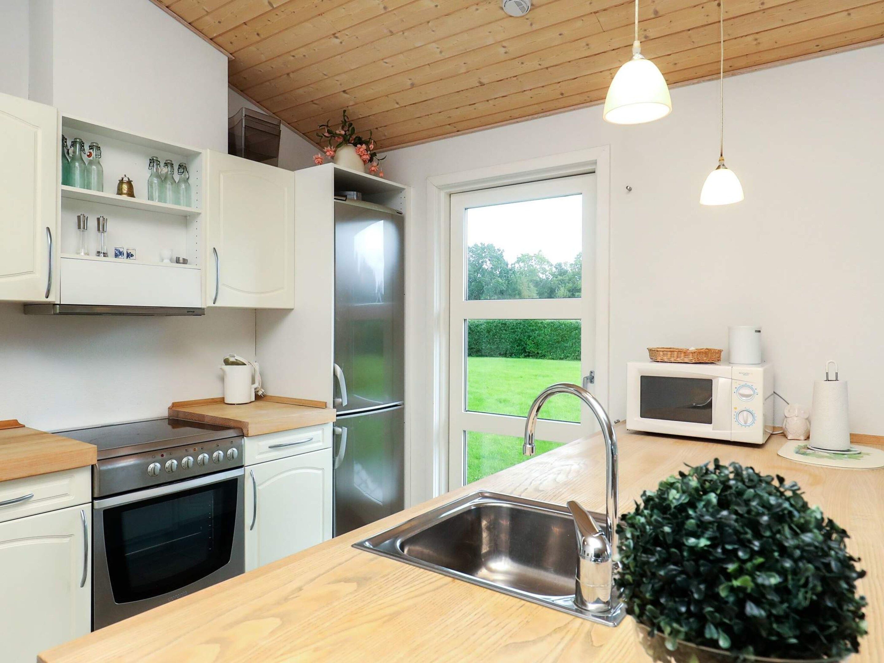 Una cocina moderna con electrodomésticos de acero inoxidable, encimera de madera y vista a un jardín verde a través de un ventanal grande.