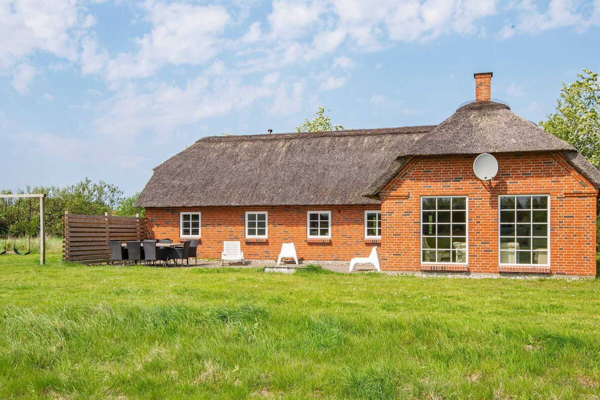 A brick house with a thatched roof, a satellite dish, and a grassy yard with outdoor seating.