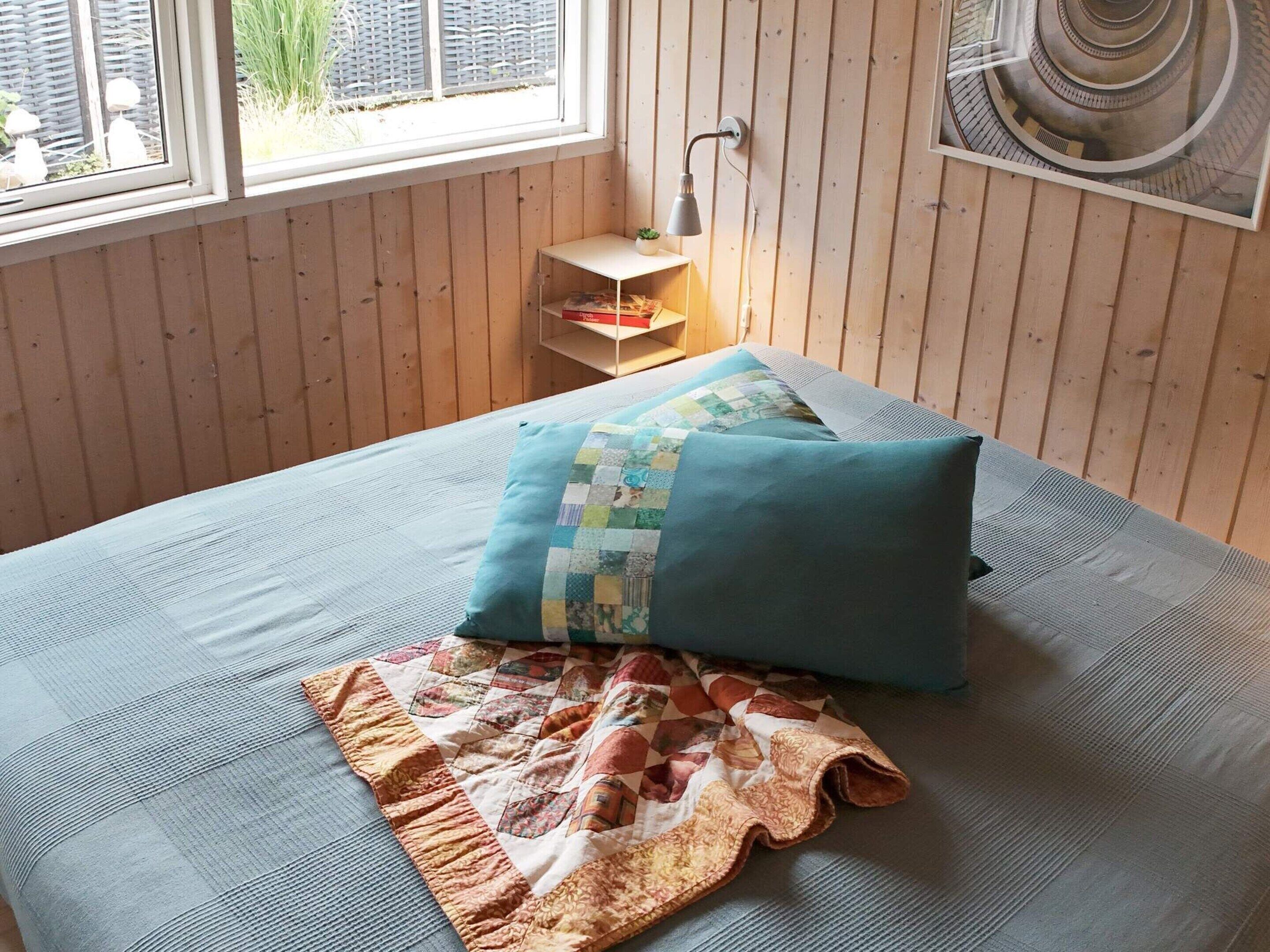 A room with a bed, a window, a small table with a lamp, and a wall-mounted picture.