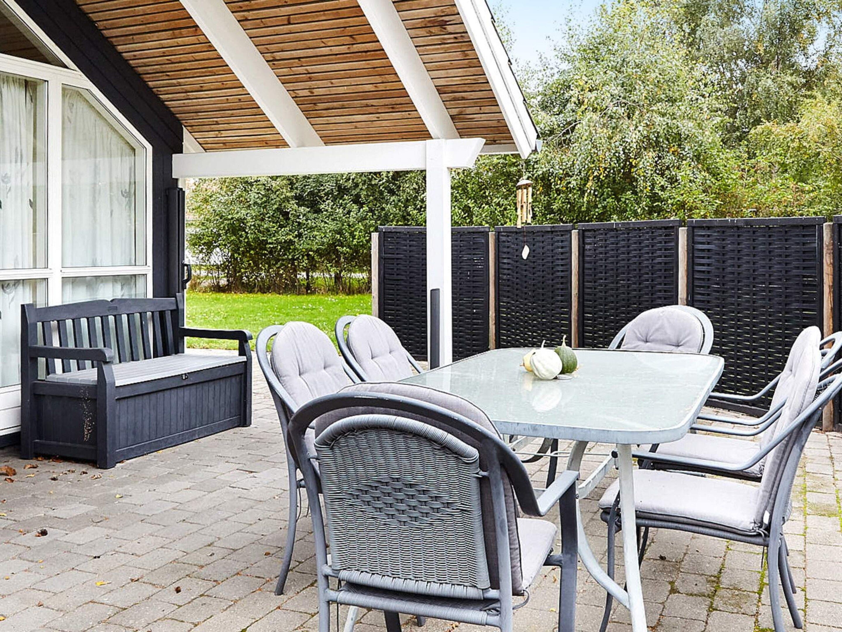 An outdoor patio with a table and chairs, a bench, and a covered area with a wooden ceiling.