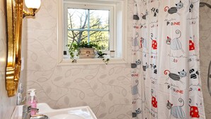 Un baño con un lavabo blanco, una ventana con una planta y una cortina de ducha con diseños de gatos.