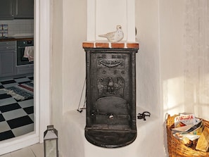 A vintage stove with a bird figurine on top, a basket with newspapers, and a checkered floor. - Holiday Home in Häradsbäck (Häradsbäck)