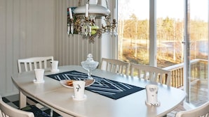 Una mesa de comedor con sillas, una araña y vistas a árboles a través de amplias ventanas.