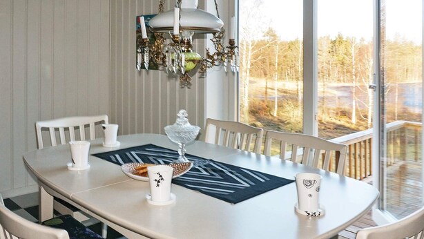 A dining table with chairs, a chandelier, and a view of trees through large windows. - Holiday Home in Häradsbäck (Häradsbäck)