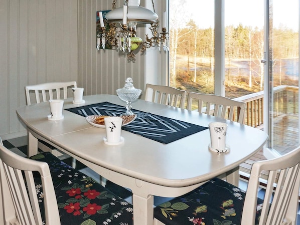 Une table à manger avec des chaises, un lustre et une vue sur les arbres à travers de grandes fenêtres.