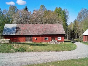 A red barn with a gravel driveway and a stack of firewood. - Holiday Home in Häradsbäck (Häradsbäck)