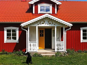 A red house with a white porch and a black dog in front. - Holiday Home in Häradsbäck (Häradsbäck)