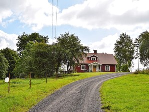 A red house with a gravel driveway leading to it, surrounded by greenery and trees. - Holiday Home in Häradsbäck (Häradsbäck)