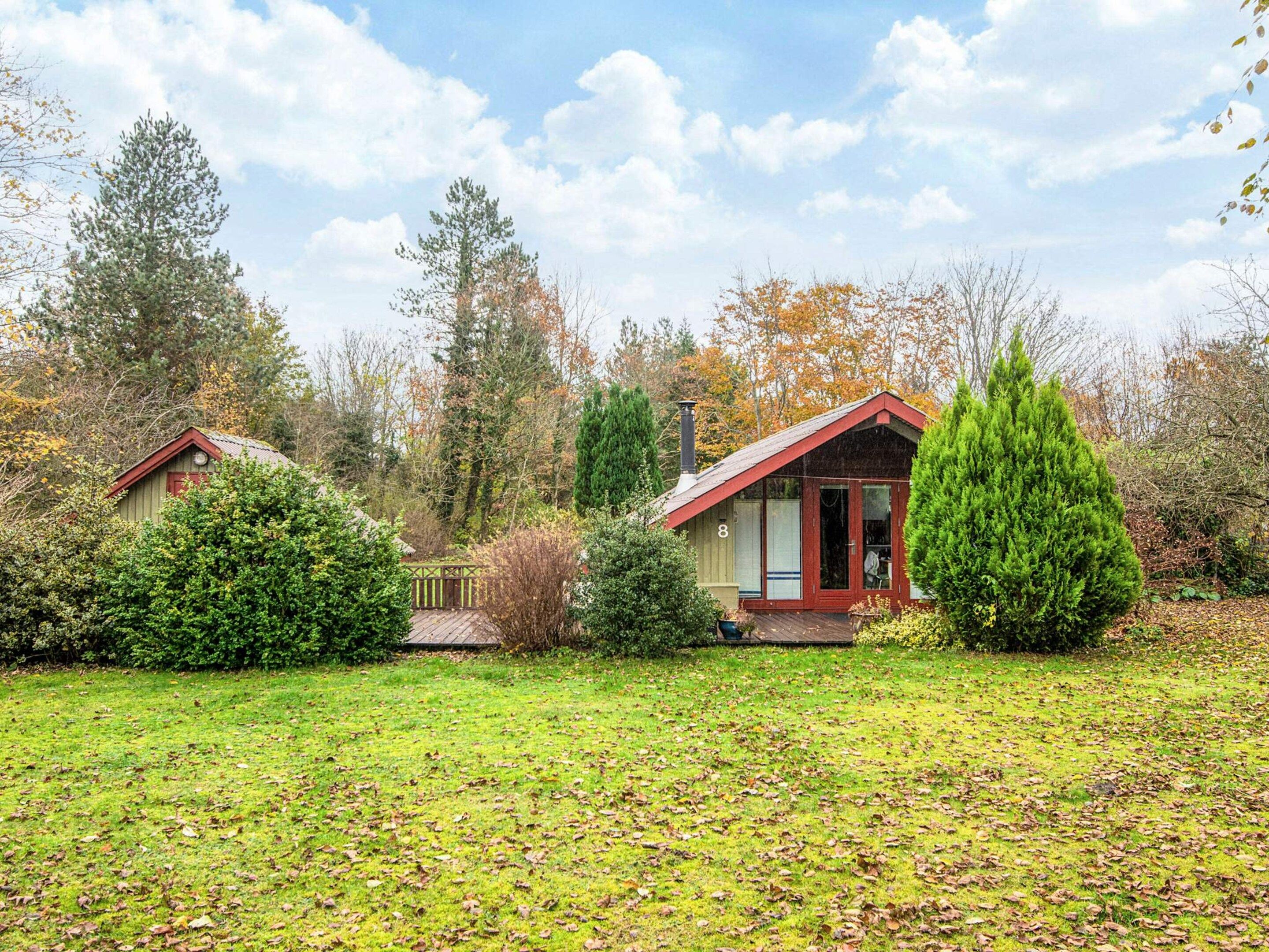 A two-story house with a red roof, surrounded by a well-maintained lawn and various trees.
