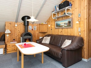 A cozy cabin interior with a brown leather sofa, a white table, a fireplace, and wooden walls. - 4 Person Holiday Home in Oksbol (Oksbol)
