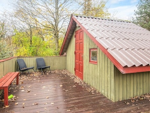 A wooden deck with two chairs and a bench, a red door, and a small window. - 4 Person Holiday Home in Oksbol (Oksbol)