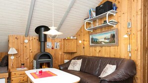 L’intérieur chaleureux d’un chalet avec un canapé en cuir marron, une table blanche, un poêle à bois et une étagère remplie de livres et ornée d’un tableau.