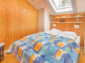A bedroom with a wooden ceiling, a skylight, a bed with a colorful quilt, a bedside table, and a shelf with decorative items. - 4 Person Holiday Home in Oksbol (Oksbol)