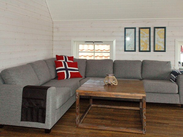 A living room with a grey sofa, a wooden coffee table, and a window with curtains. - Holiday Home in Urangsvåg (Bomlo)