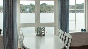 A dining area with a round table and white chairs, a decorative lantern, and a view of a lake through large windows. - Holiday Home in Urangsvåg (Bomlo)