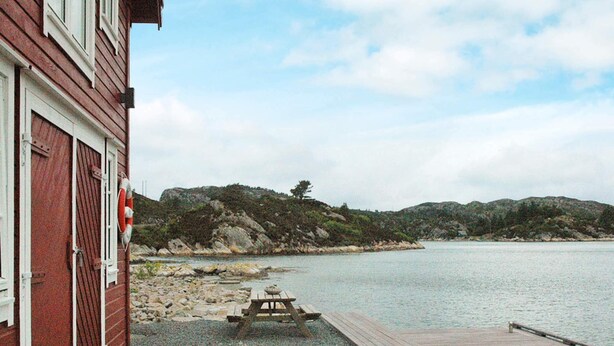 A wooden dock extending into calm waters, a picnic table, and a red building with white trim. - Holiday Home in Urangsvåg (Bomlo)