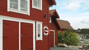 A red building with two garage doors, a lifebuoy attached to the wall, and a gravel driveway. - Holiday Home in Urangsvåg (Bomlo)