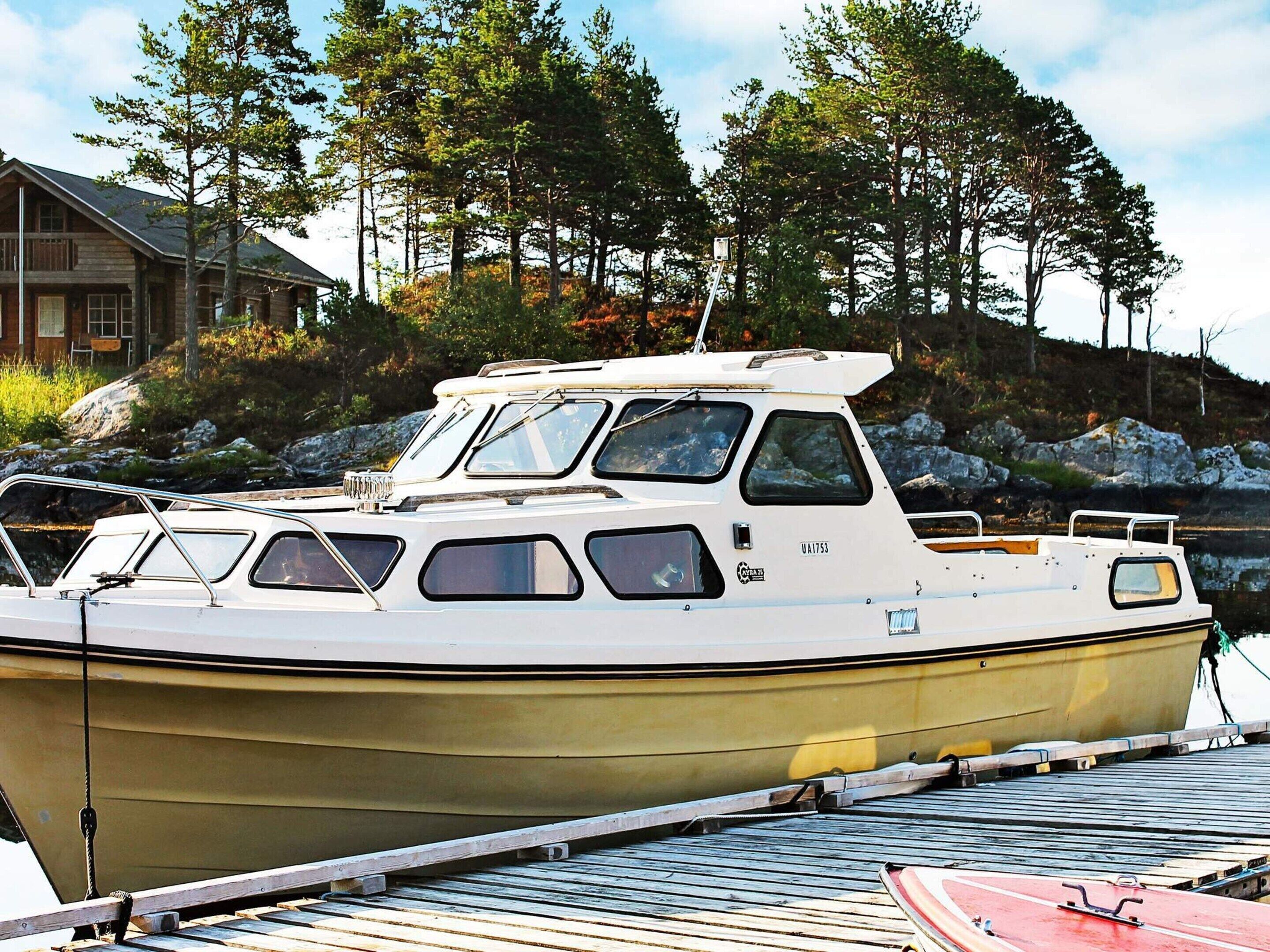 A small, white motorboat docked at a pier with a rocky shoreline and trees in the background.